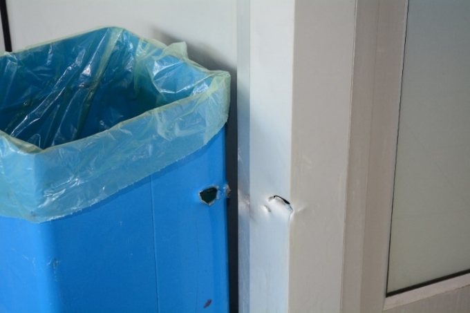 Apparent bullet hole through garbage can and corner of security office.  