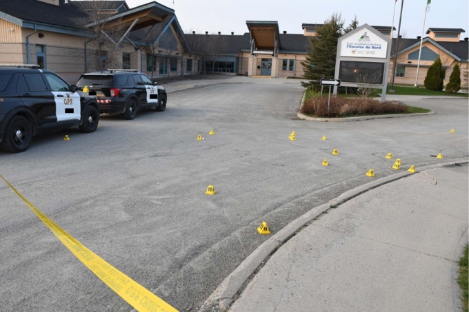 Figure  1 – École secondaire catholique L’Envolée avec deux voitures de la Police provinciale et plusieurs marqueurs de preuve jaunes dans l’entrée 